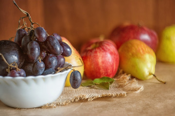 Autumn harvest. Plate of ripe blue grapes on a background with red apples and with yellow pears.