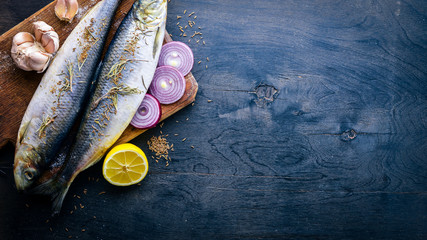 Fresh fish with vegetables, spices and oil. On a black wooden background. Free space for text . Top view