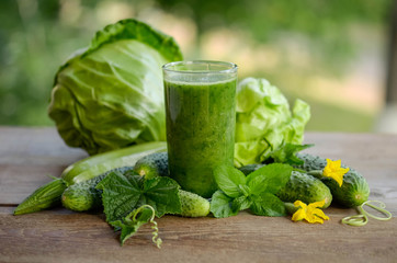  glass with green smoothie on a wooden table and  vegetables with mint leaves