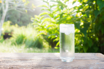Close up glass of cold water with ice on table with blur garden background