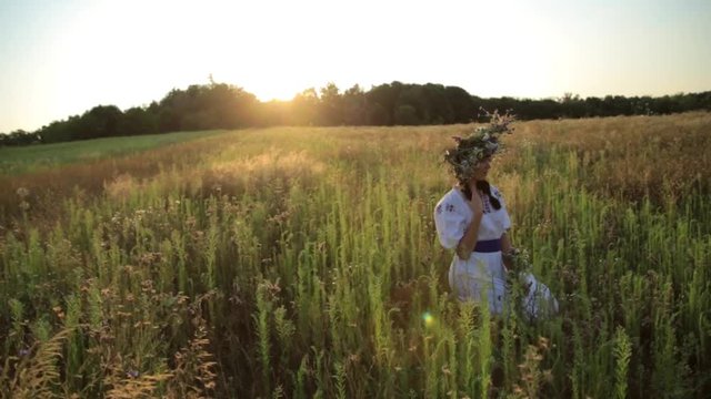 Girl walking in meadow wearing flower circlet and ethnic outfit at sunset in nature.