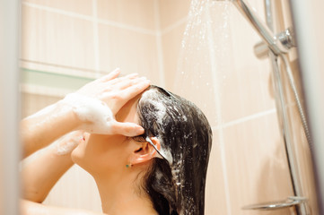 Beautiful naked young woman using shampoo while taking shower in bathroom