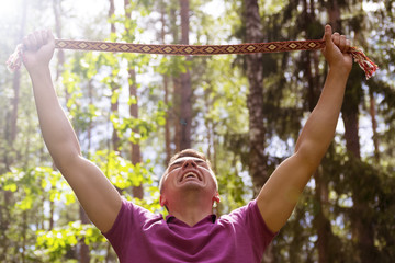 Fototapeta premium A young man holding a ribbon with the ornament above his head and shouts. The national ornament of the Republic of Belarus.