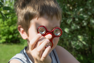 Fidget red spinner stress in hand.  Young boy play with red fidget spinner in outdoors, focus on spinner.