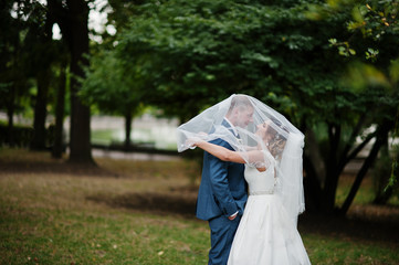 Wedding couple posing under bridal veil outdoor.