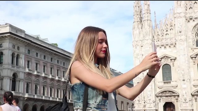 Beautiful teenager tourist girl taking a photo with her mobile phone. Photo taken in Milan, Italy