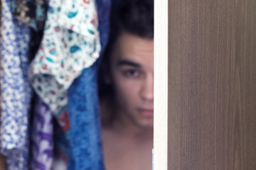 A young man hiding in the closet among women's clothing. Lover in the closet.