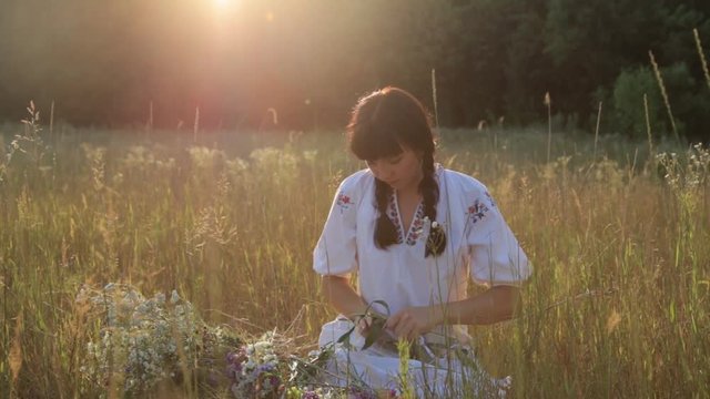 Girl making flower circlet in the meadow at sunset in nature.