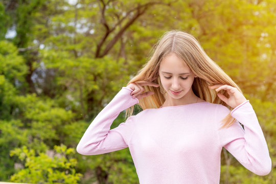 Blonde funny happy pretty girl in a pink sweatshirt in the park. Portrait close up. Sunny day