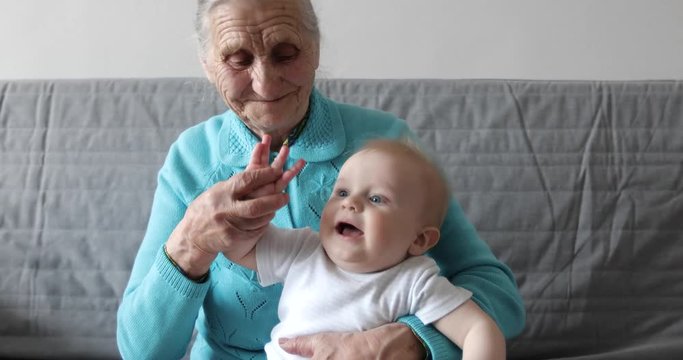 An elderly grandmother holds a small grandson in her arms and plays with him.