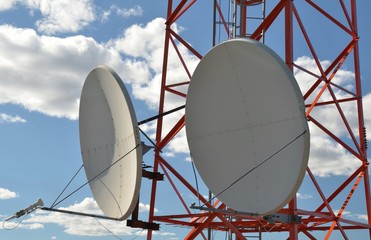Two huge satellite dishes, mounted on television tower, against blue cloudy sky. Fragment
