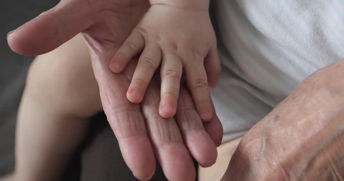 Old wrinkled hands touching the baby's soft hands.