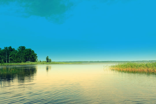 Beautiful natural summer calm water landscape: a forest lake against a blue sky on a sunny clear day, perspective. Relaxation, pacification.Best fairy nature .Toned image