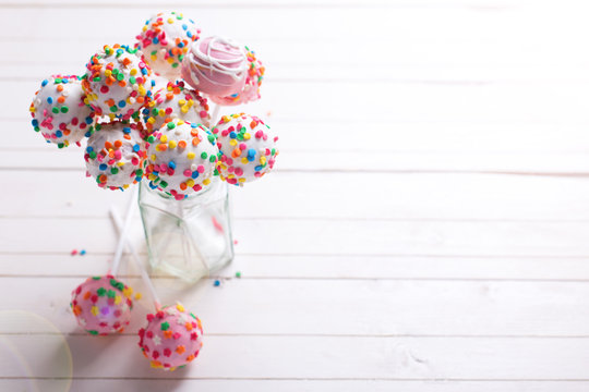 Colorful bright cake pops  in  jar on  white wooden   background.