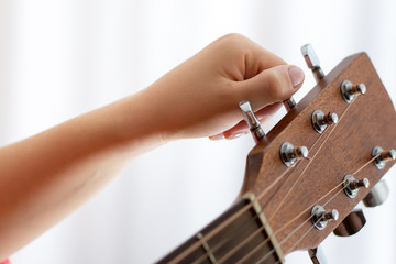 Photo of girl's hand tuning acoustic guitar, close-up