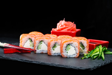 Traditional Japanese cuisine. Selective focus on Philadelphia sushi rolls with salmon, cream cheese, rice and cucumber on dark background, near ginger and sliced cucumber