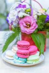 Fototapeta na wymiar Summer flowers bouquet in a basket, white red and purple. Pink and green macaroons sweets and candies on white plate