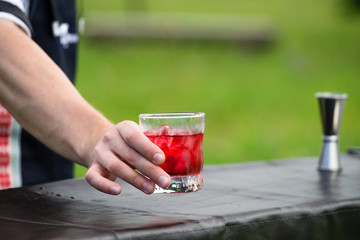 bartender workplace. Selective focus on a bartender who holding a glass with red cold cocktail. Concept of preparation cocktail, bar catering service and small business