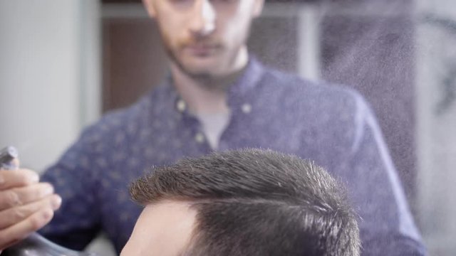 Close up of male head with the barber spraying water on hair of client and brushing it making haircut. Hairdresser working at the barbershop doing undercut with comb and hair styling products.