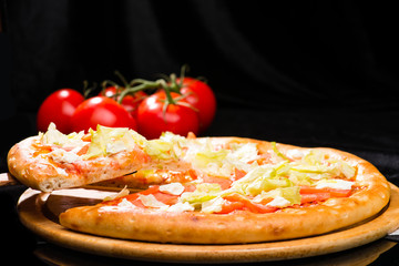 appetizing Italian pizza with tomatoes and cabbage leaves and sliced piece on wooden board, dark background, selective focus