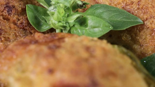 Crocchette di zucchine e mollica di pane con basilico fresco in un piatto rotante.