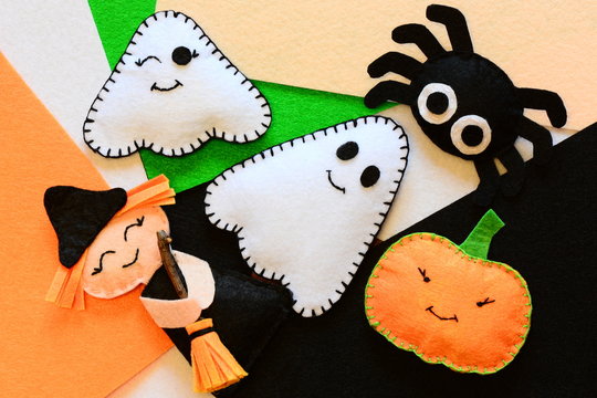 Halloween cute felt ornament decor. Small witch with broom, pumpkin head, two ghosts, spider. Halloween toys crafts on colored felt pieces. Simple kids sewing crafts concept. Top view