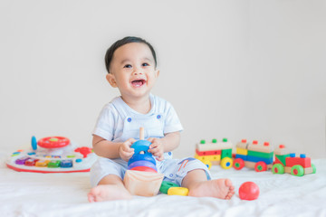 Adorable Asian baby boy 9 months sitting on bed and playing with color developmental toys at home..
