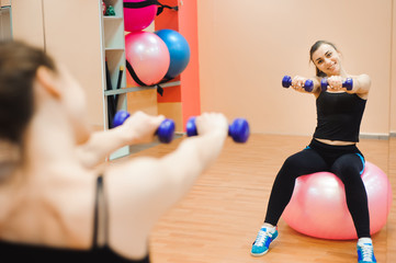 Fototapeta na wymiar Young woman in sportswear, doing fitness exercise with fit ball and dumbbells.