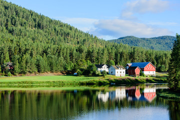 Obraz premium Small village with two main houses and some farm buildings situated in forest landscape at a tranquil river bend. Location Skutsvika along route 40 in Norway.