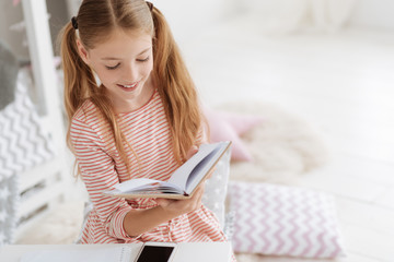 Smiling schoolgirl with ponytails reading book at home