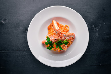 Pasta and tiger shrimp in tomato sauce. Italian traditional food. On a wooden background. Top view. Free space for your text.