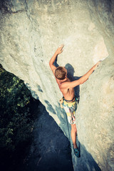 Men climbs an overhanging rock and forest  on the background