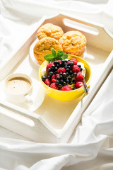 Wooden tray with tasty breakfast on bed. Espresso, banana muffins, cottage cheese with blueberry and raspberry. Sun light. Selective focus