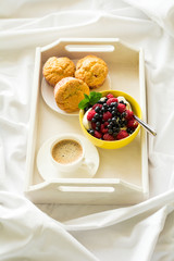 Wooden tray with tasty breakfast on bed. Espresso, banana muffins, cottage cheese with blueberry and raspberry. Sun light. Selective focus