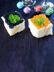 Canape with red and black caviar and wine glasses with Christmas decorations in the background