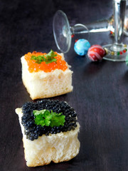Canape with red and black caviar and wine glasses with Christmas decorations in the background