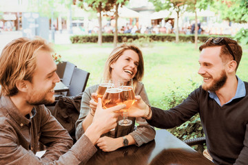 Group of smiling young friends clanging glasses of beer