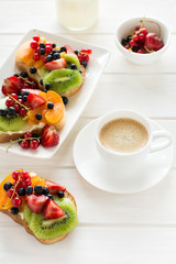Espresso and fruit dessert sandwiches with ricotta cheese, kiwi, apricot, strawberry, blueberry and red currant on white wooden table. Selective focus