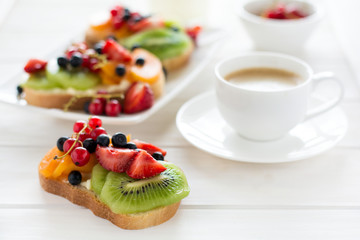 Espresso and fruit dessert sandwiches with ricotta cheese, kiwi, apricot, strawberry, blueberry and red currant on white wooden table. Selective focus