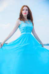 Fototapeta na wymiar Gorgeous woman in long beautiful flying dress. Elegant girl in fluttering dress. Fashion style portrait. Young elegant woman posing at yacht against bridge. Consent of femininity and tenderness
