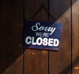  Sorry we're closed, blue and white retro sign on old wooden door, with a shadow that divides it into a clear and dark part