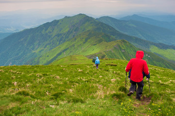 Travelers descending down a winding path leading to majestic green mountain peak and hills covered...