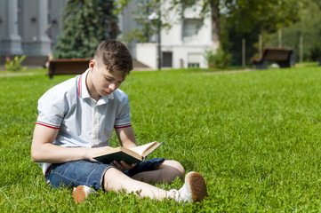 Fototapeta premium Young man reading a book sitting on the grass