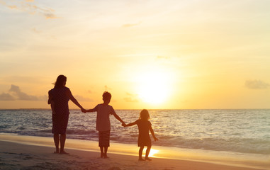Fototapeta na wymiar mother with three kids walking on beach at sunset