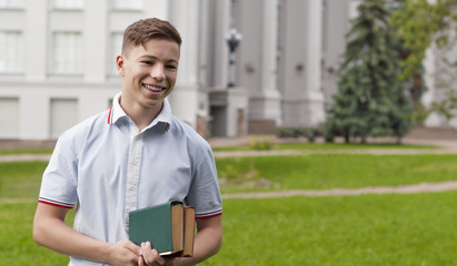 Young man with a book in his hands near the gray building