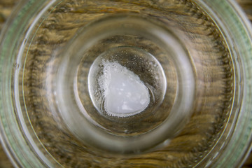 Top down close up view on coco oil dissolving in clear glass container over wooden background