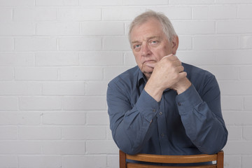 Serious mature man with a white brick background and copy space 