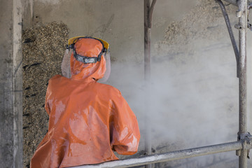 Worker in orange protective suit cleans corrosion damaged concrete bridge pillar with high pressure washer