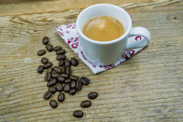 Coffee beans alongside a cup of milk coffee placed on a napkin on a cloth with copy space