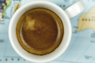 Cup of freshly brewed espresso coffee viewed close up from above on a world map background
